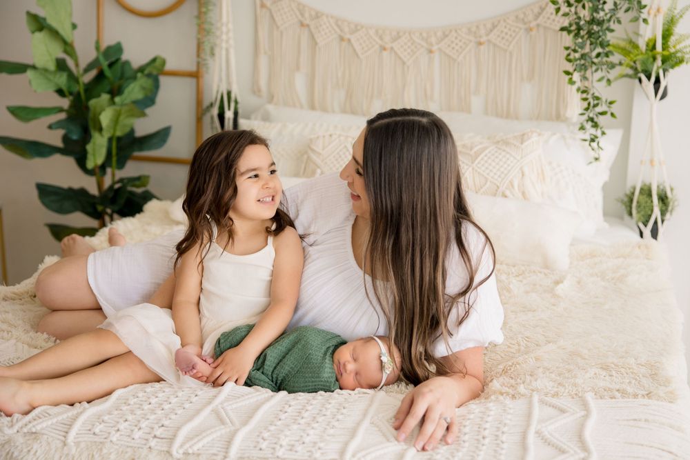Family members sharing joyful interaction while relaxing on white bed with macrame wall decor.