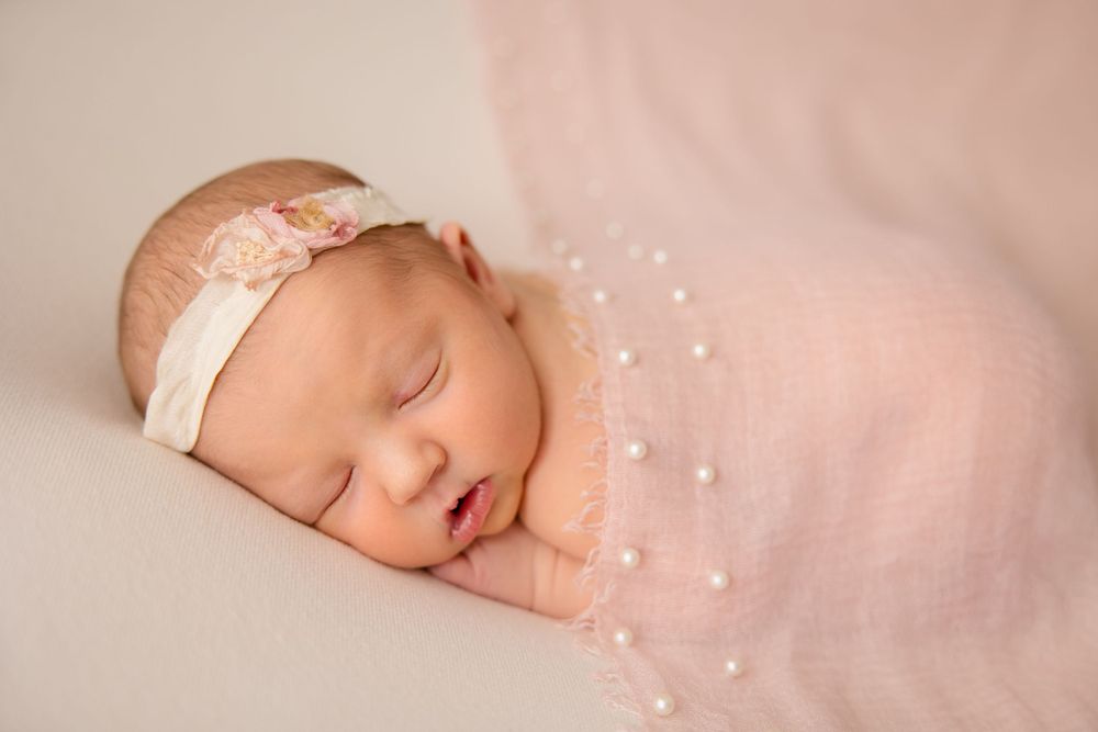 Dreaming newborn with lace headband against pink backdrop with sparkle overlay.
