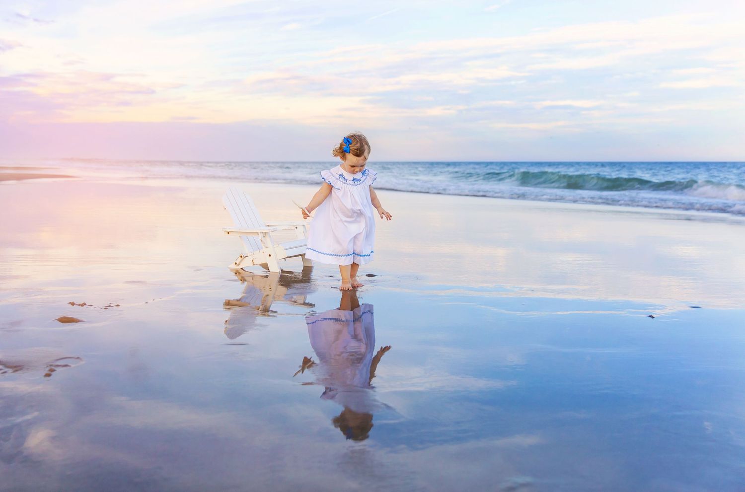 People walking along a serene beach at sunset creating reflections in the wet sand.