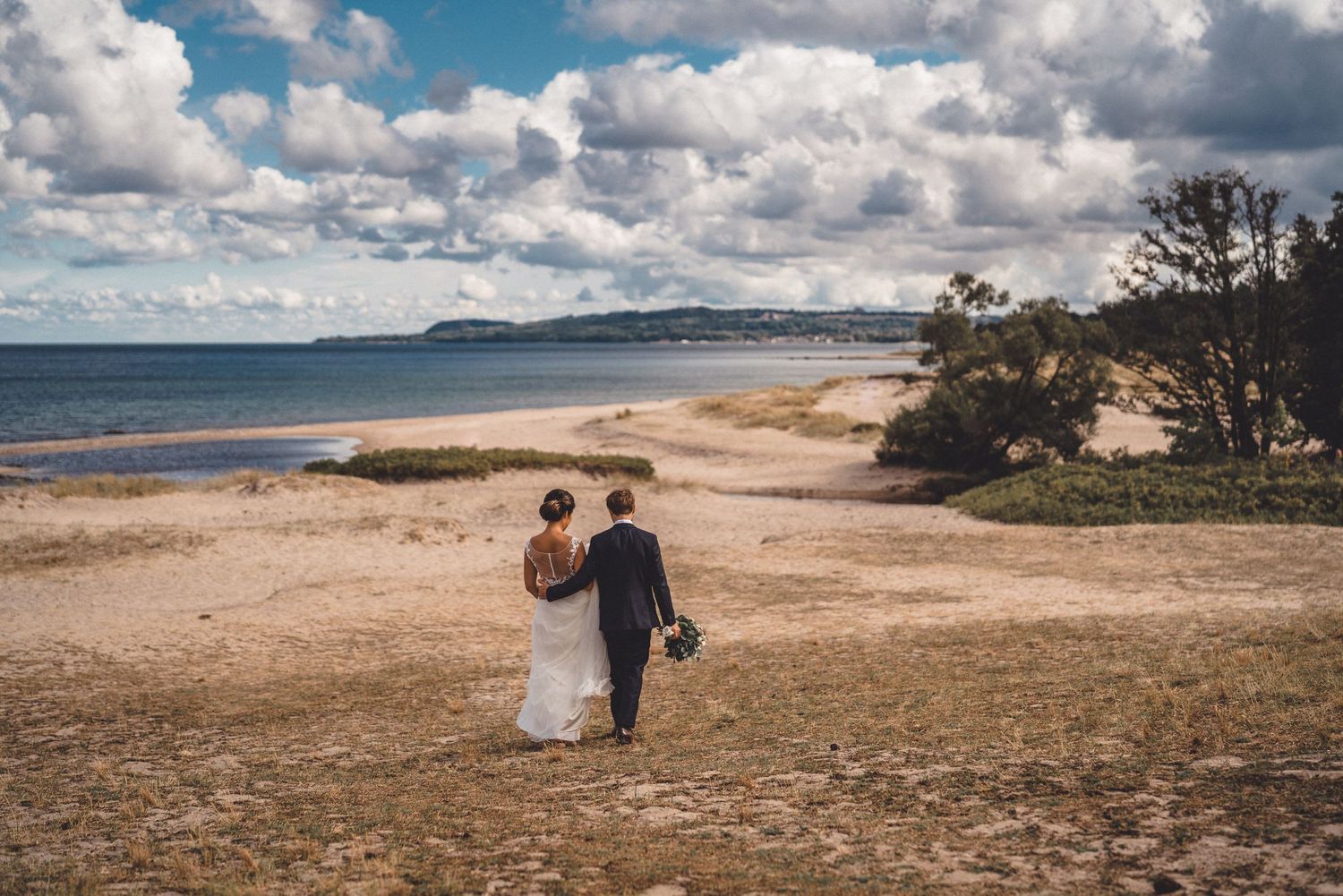 Brudpar går mot strandkanten i Kivik och Havängs strand en molnig sommardag
