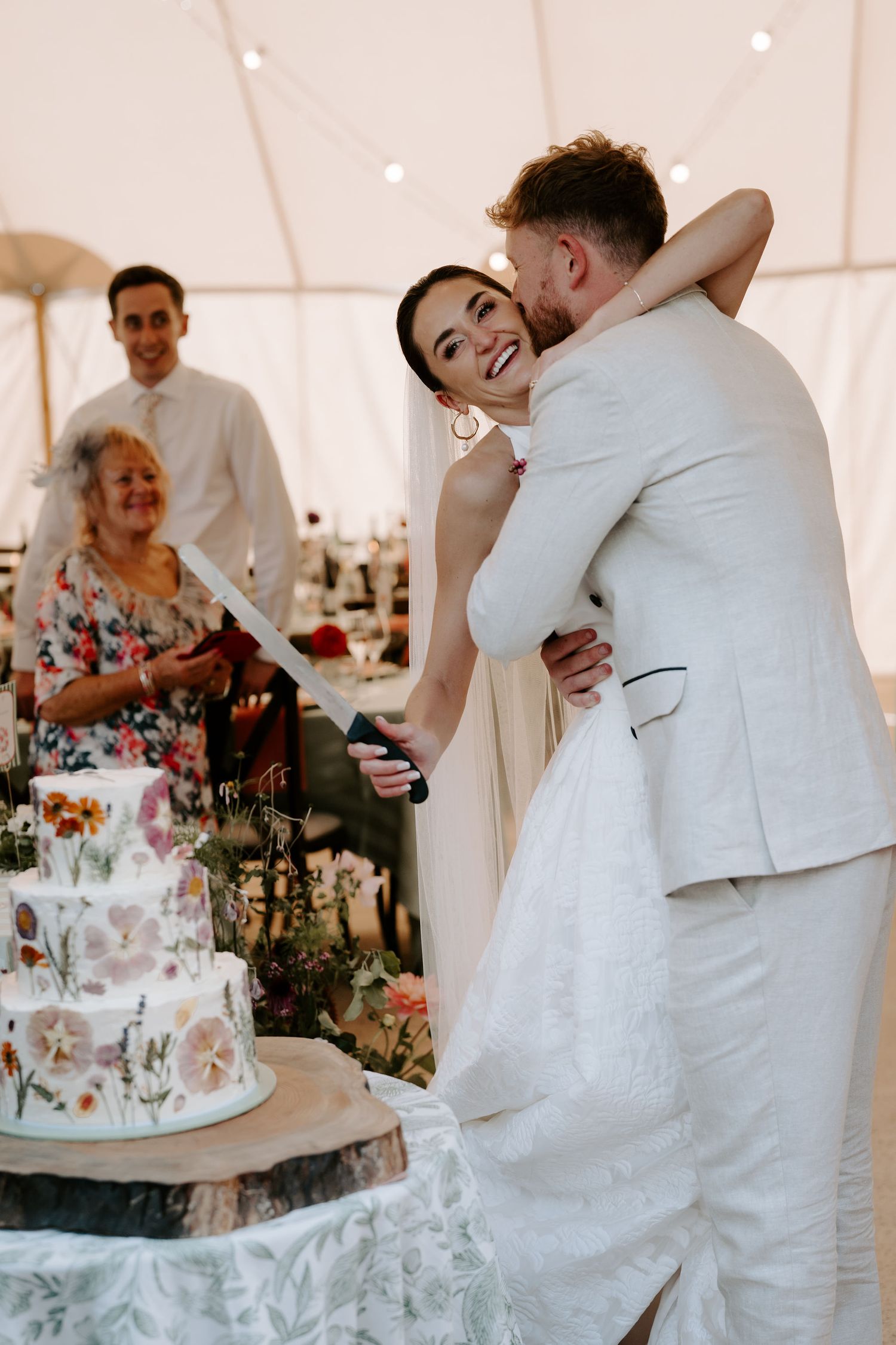 bride smiling over the grooms shoulder before cutting the cake at marquee wedding in islip in Oxfordshire
