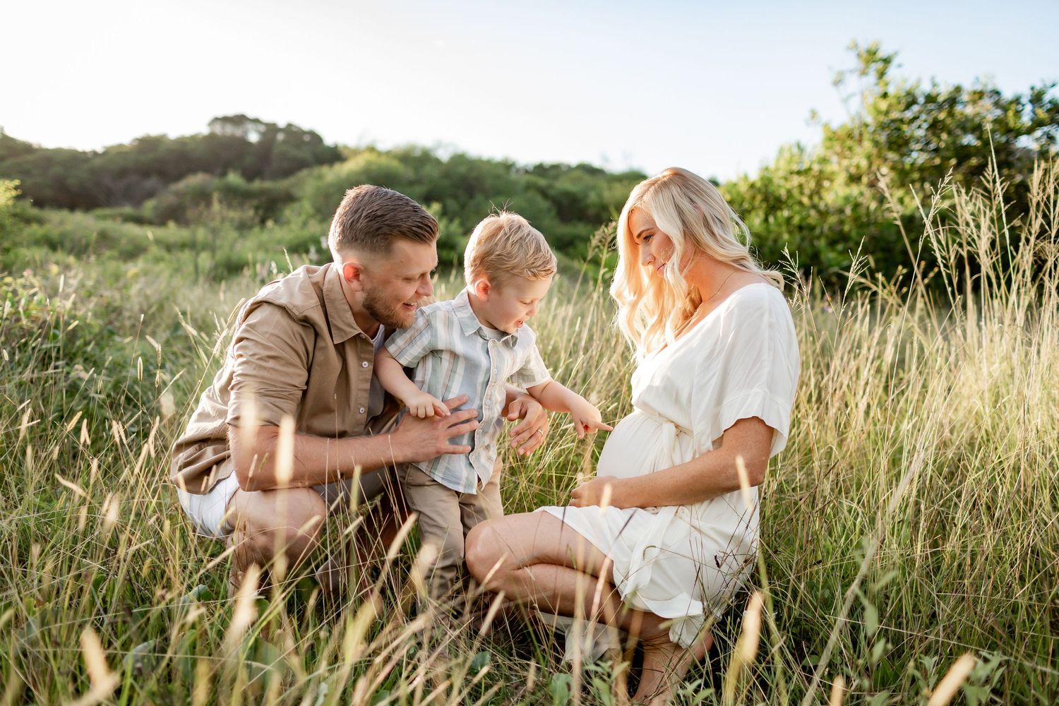 Family sharing an intimate moment while kneeling together in a field of tall grass.