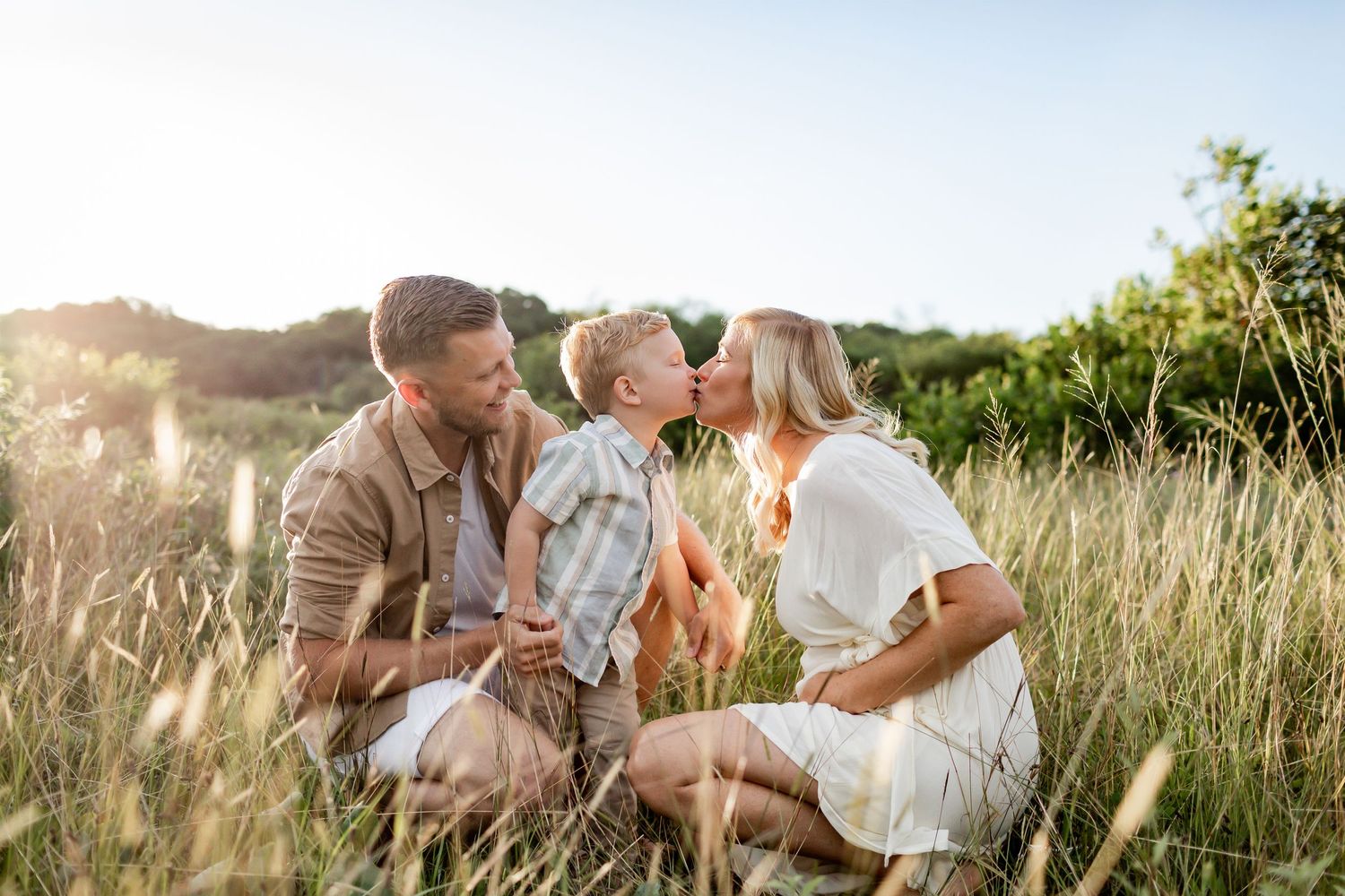 Sweet family moment captured in golden sunlit field with natural vegetation.