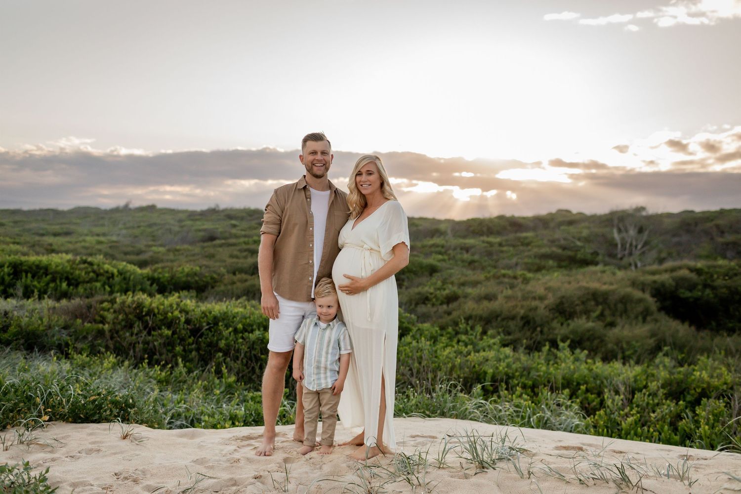 Family maternity photo taken at sunset on rocky overlook with scenic landscape behind.