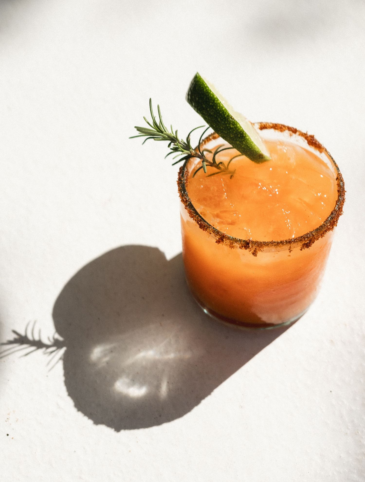 Orange cocktail garnished with lime and herbs served in a glass with spiced rim.