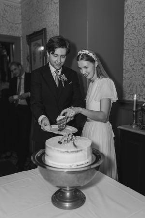 A vintage black and white wedding photo of a couple cutting their wedding cake.