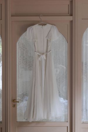 An elegant white wedding dress hanging on display against a beige door.