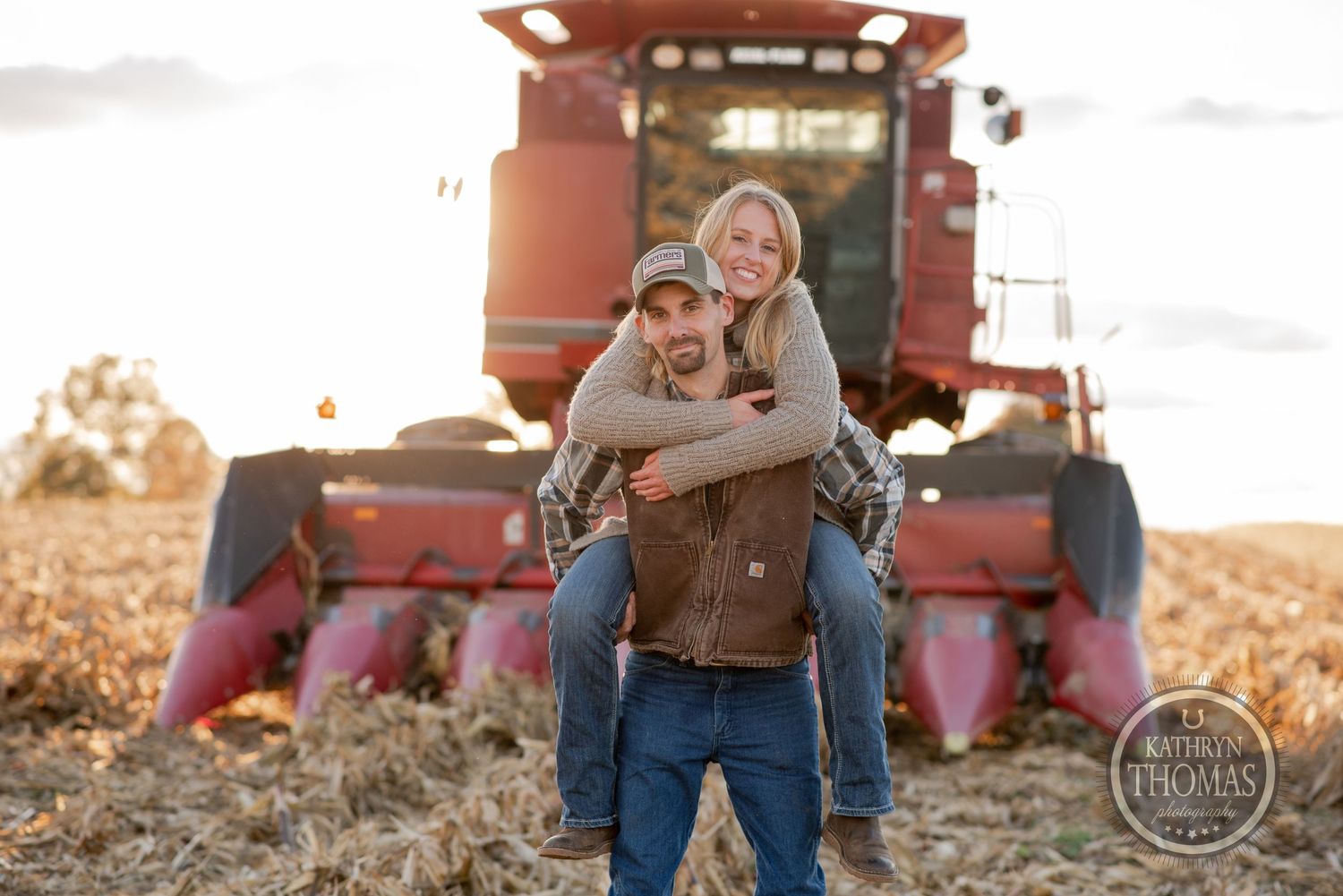 Playful couple having fun in front of farm equipment at sunset.