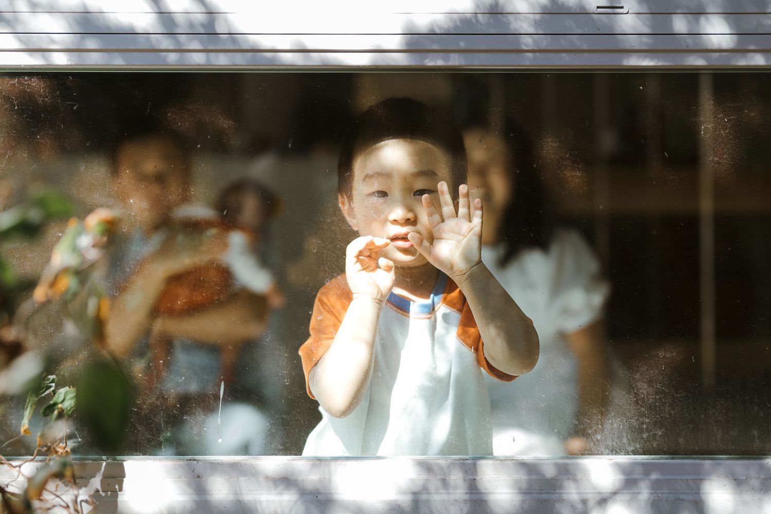 Child looking through a window making a playful face gesture on a sunny day.