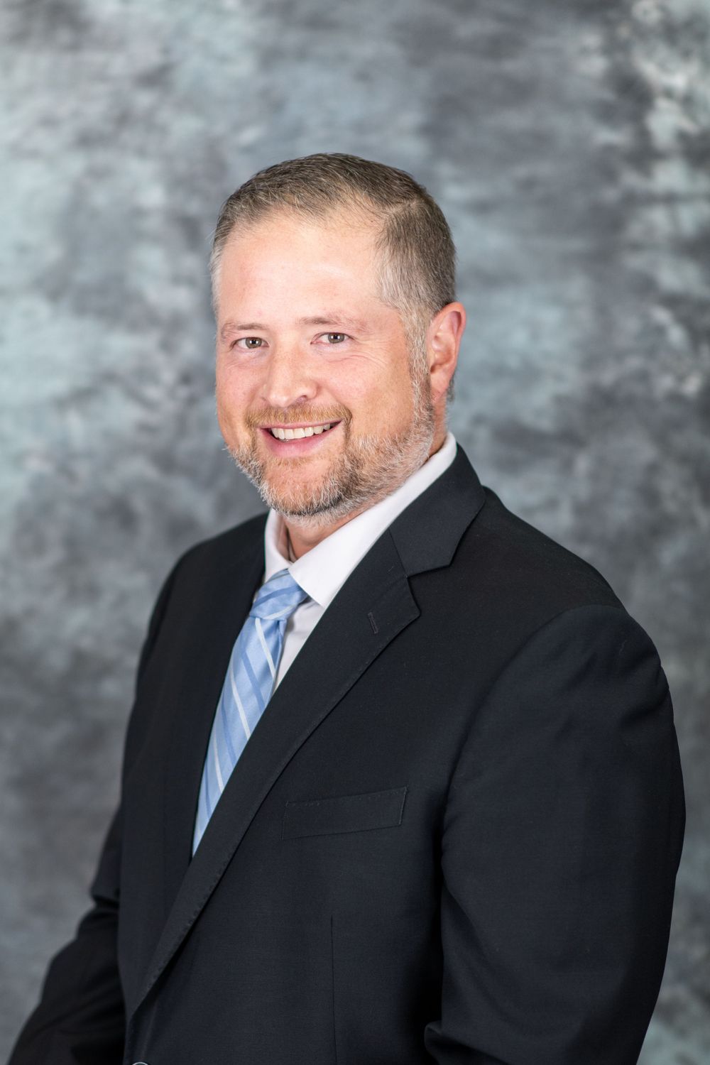 Professional portrait series in black suit and blue tie against grey backdrop.