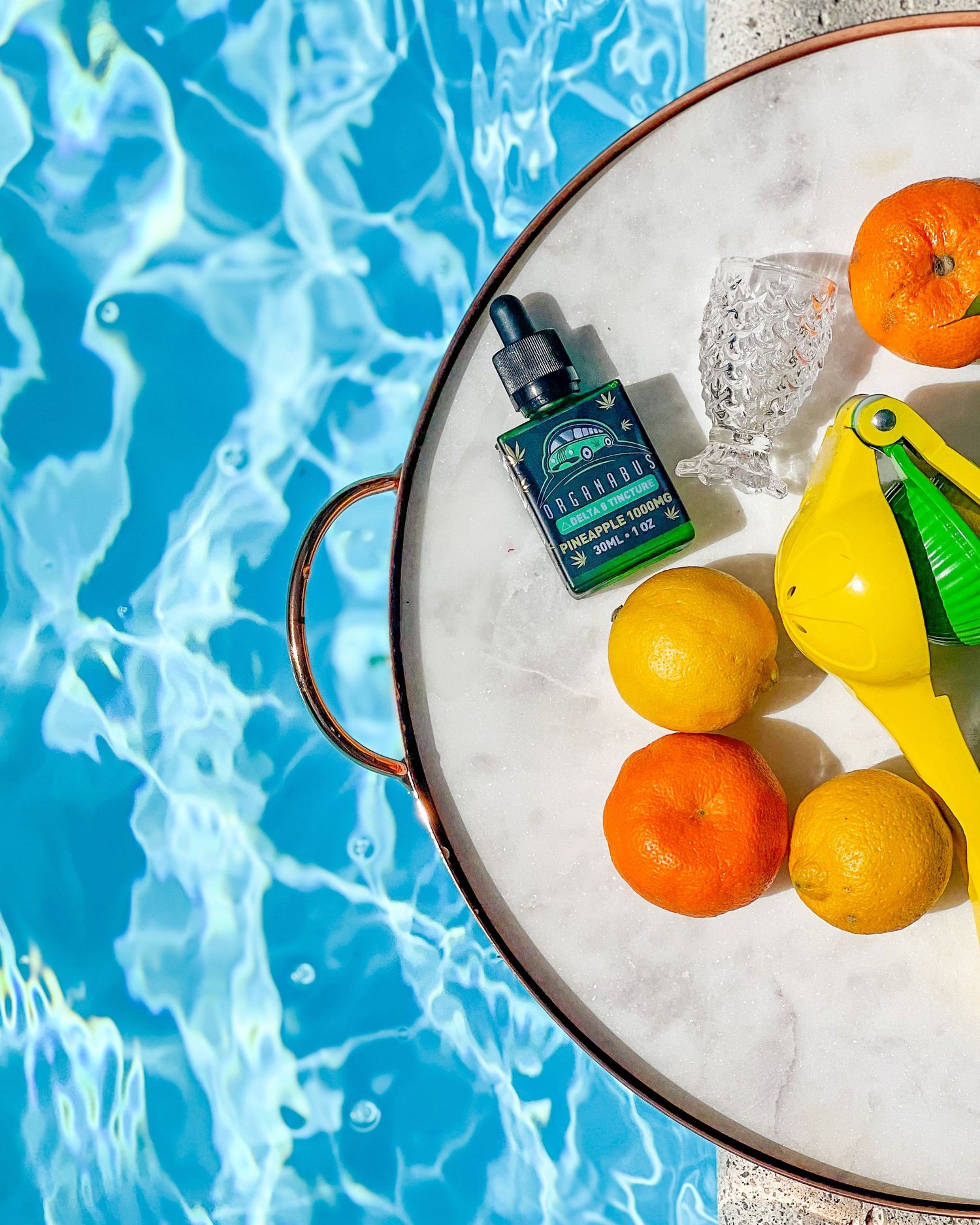 CBD oil drops bottle with fresh citrus fruits on marble tray beside a sparkling blue pool.