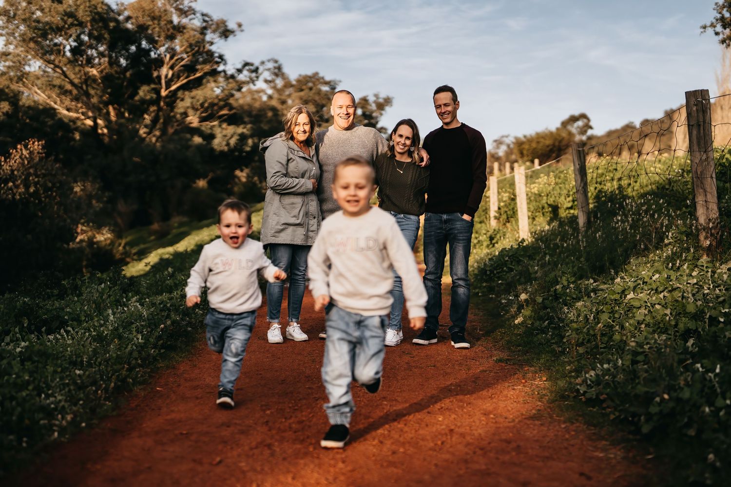 Family members walking and playing together on a red dirt path surrounded by greenery.