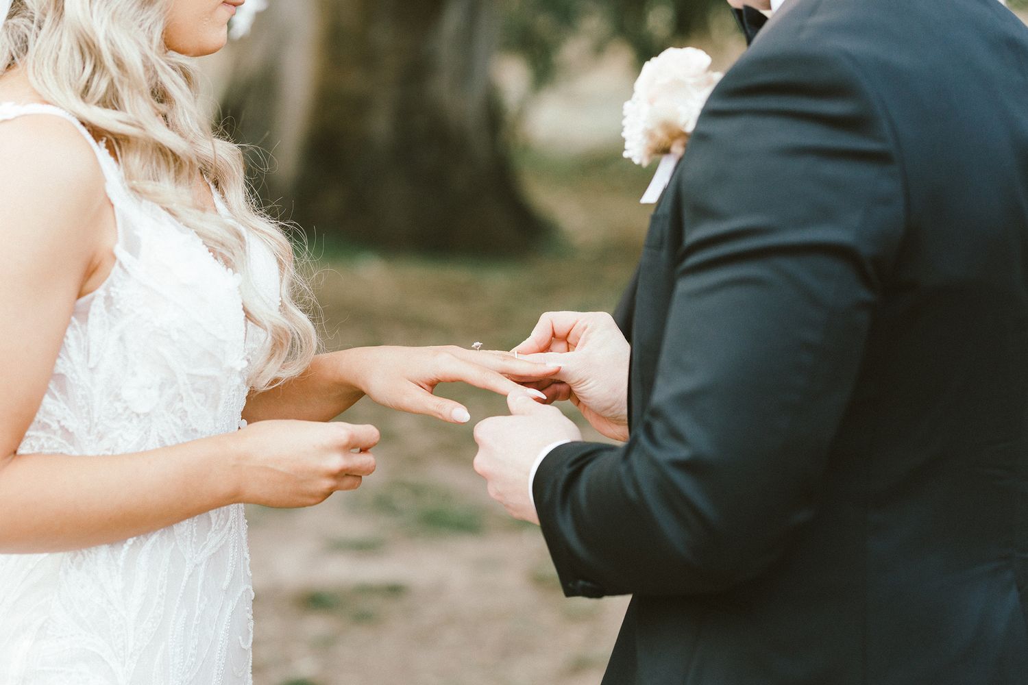 Close-up of hands exchanging rings during an elegant outdoor wedding ceremony.