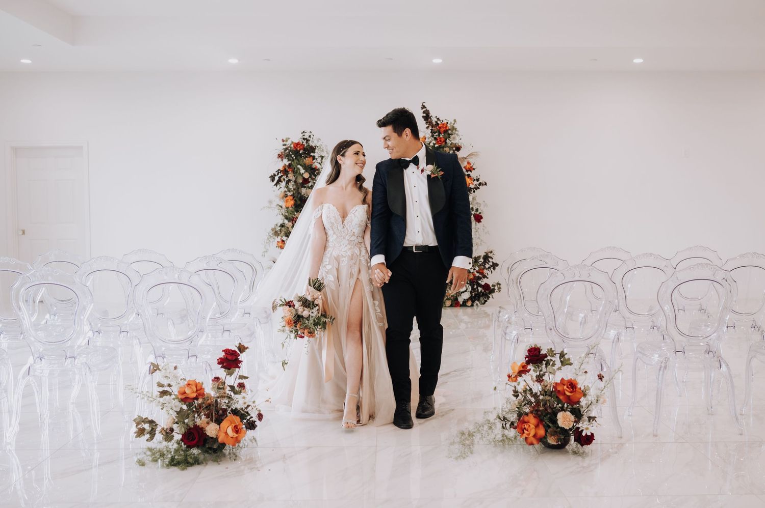 Wedding couple walking through modern white venue decorated with floral arrangements.