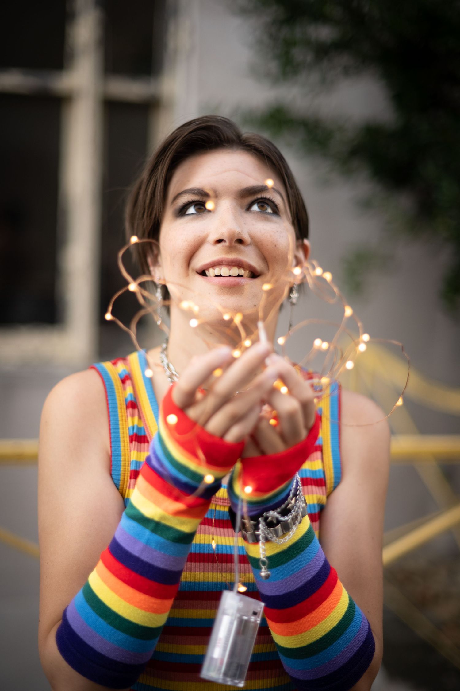 A joyful portrait with rainbow arm warmers and twinkling fairy lights creating a magical atmosphere.