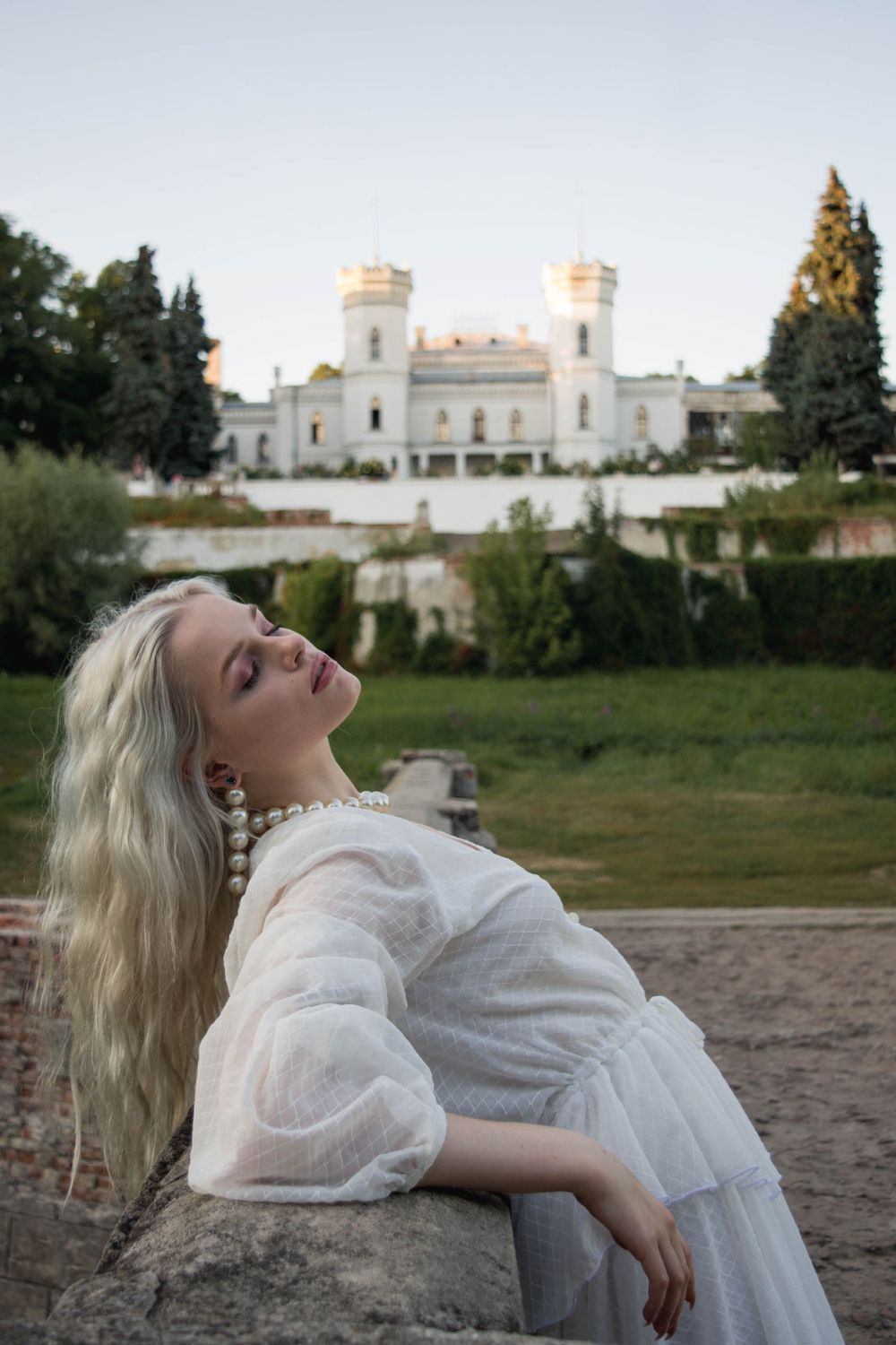 White castle with twin towers provides backdrop for dramatic portrait on grassy hillside.