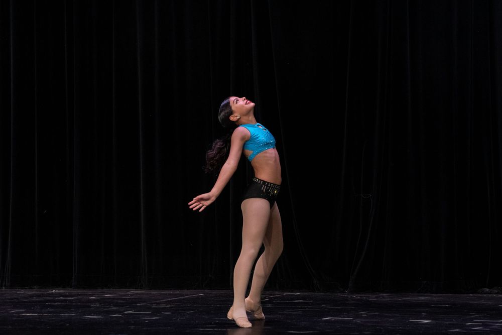 Modern dancer stretches gracefully across stage floor in dramatic lighting.