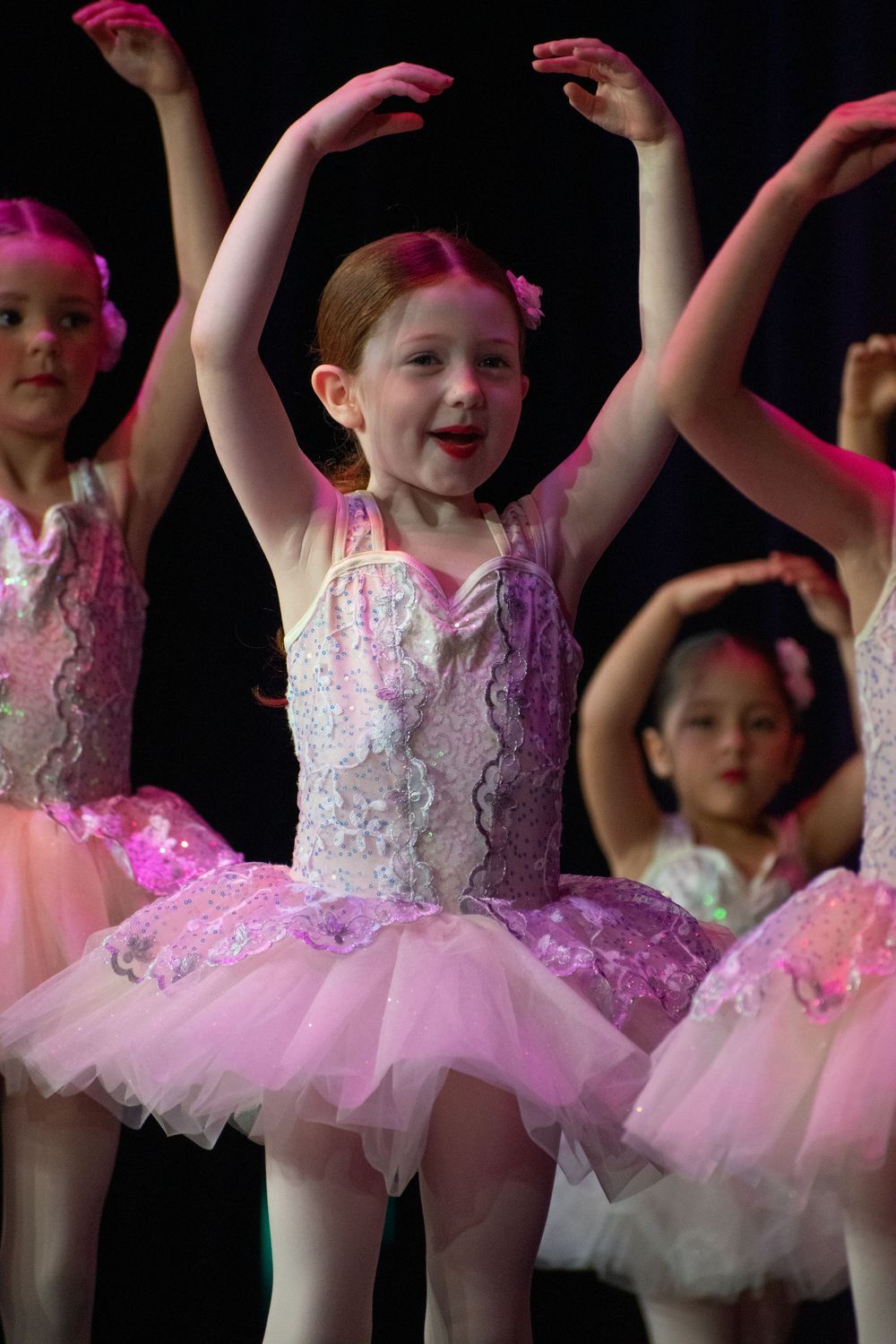 Performers in pink and white tutus strike ballet poses during recital.