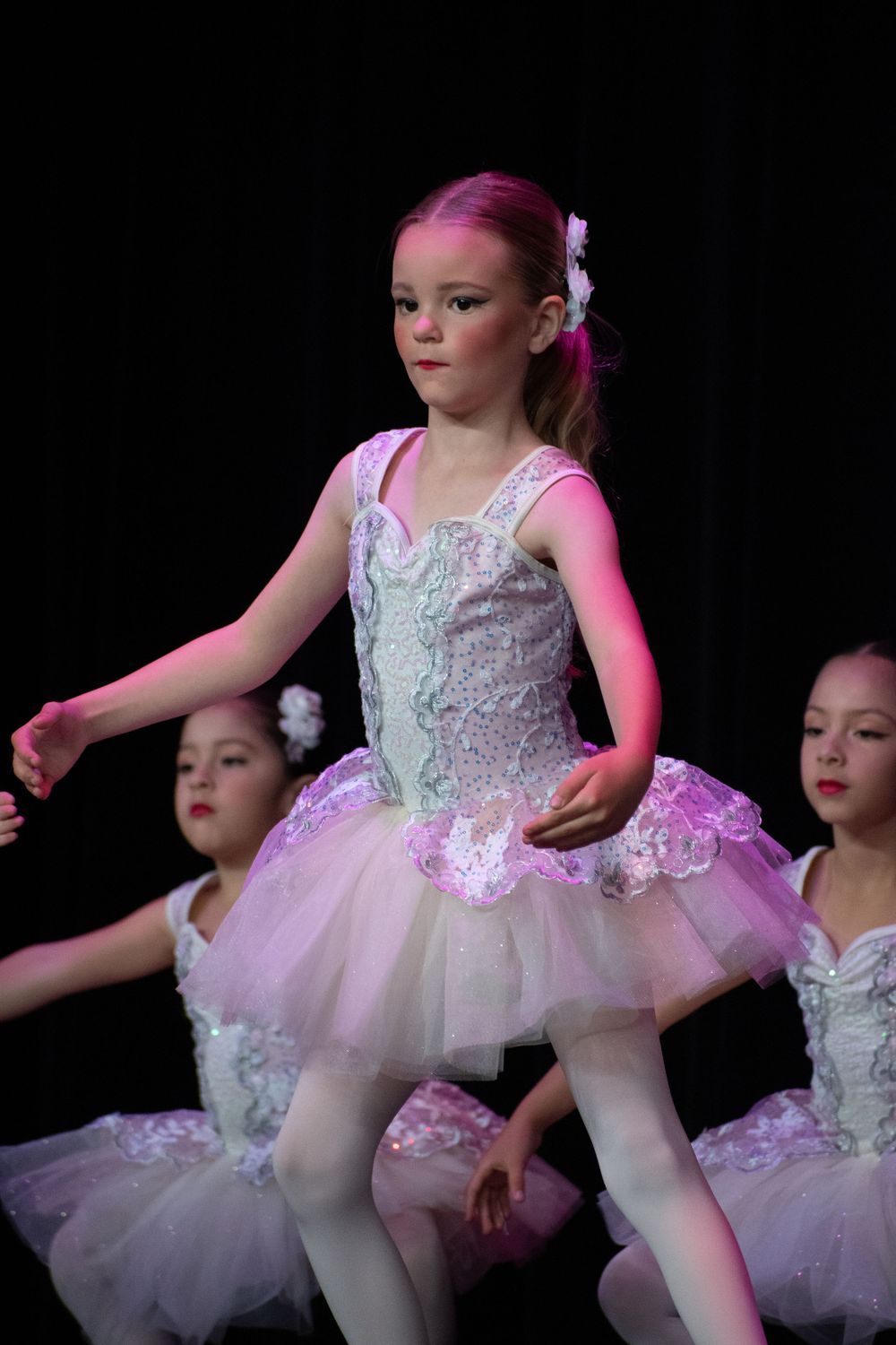 Ballet dancers in white tulle tutus perform graceful movements under stage lights.