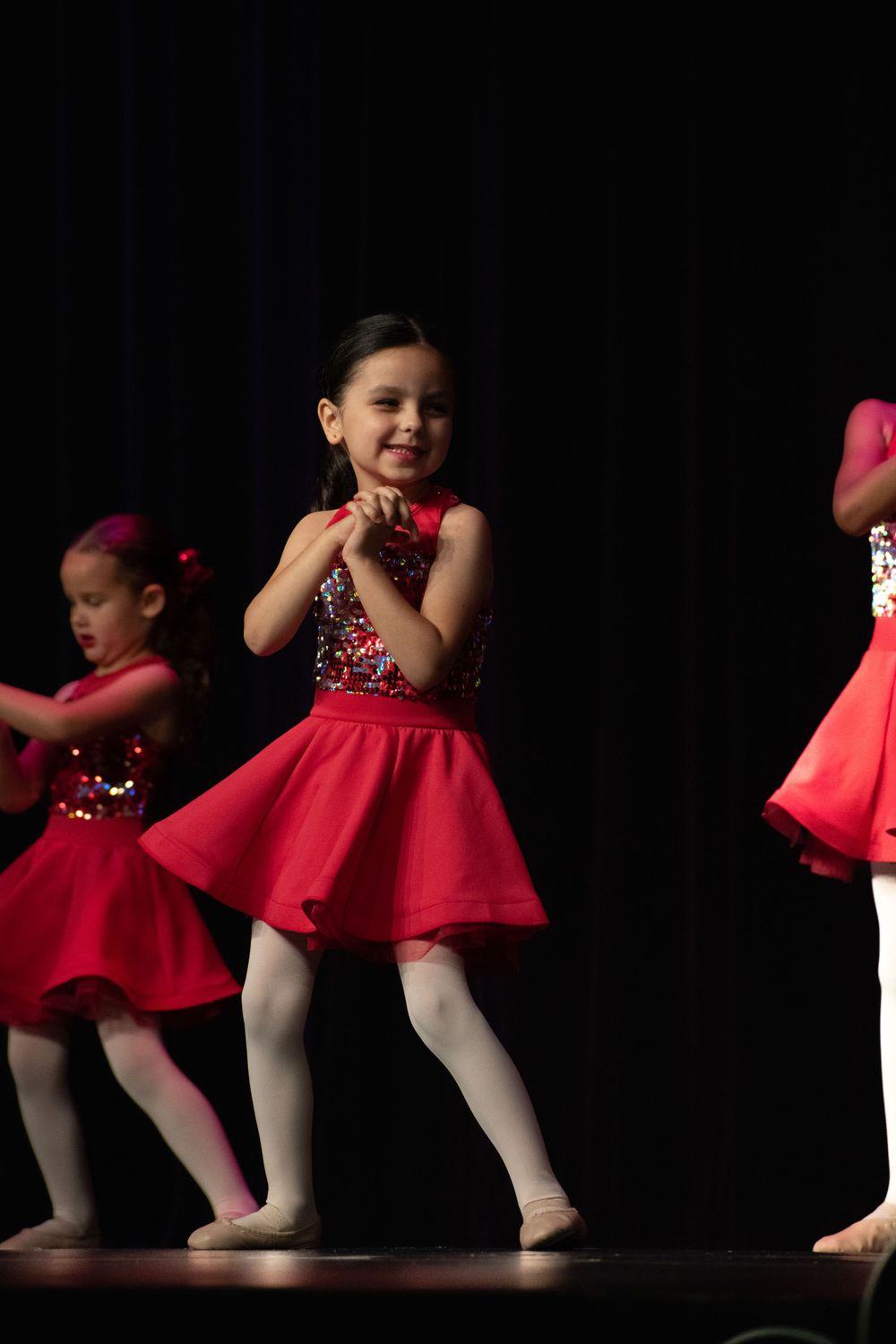 Young performers in red sequined dresses dance in synchronized line formation.