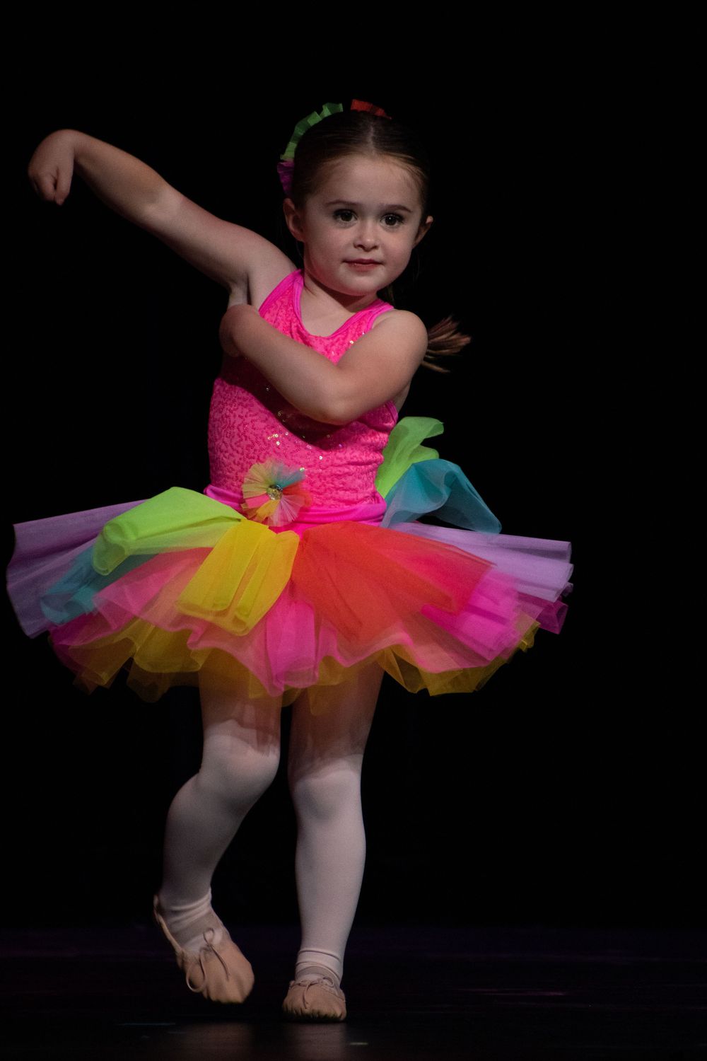 A dancer twirls in a colorful rainbow tutu and neon pink leotard during a performance.