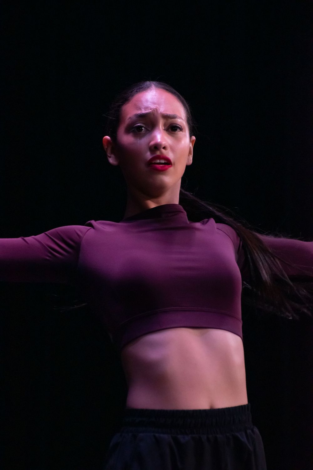 Contemporary dancer in purple crop top performs expressive movement on stage.