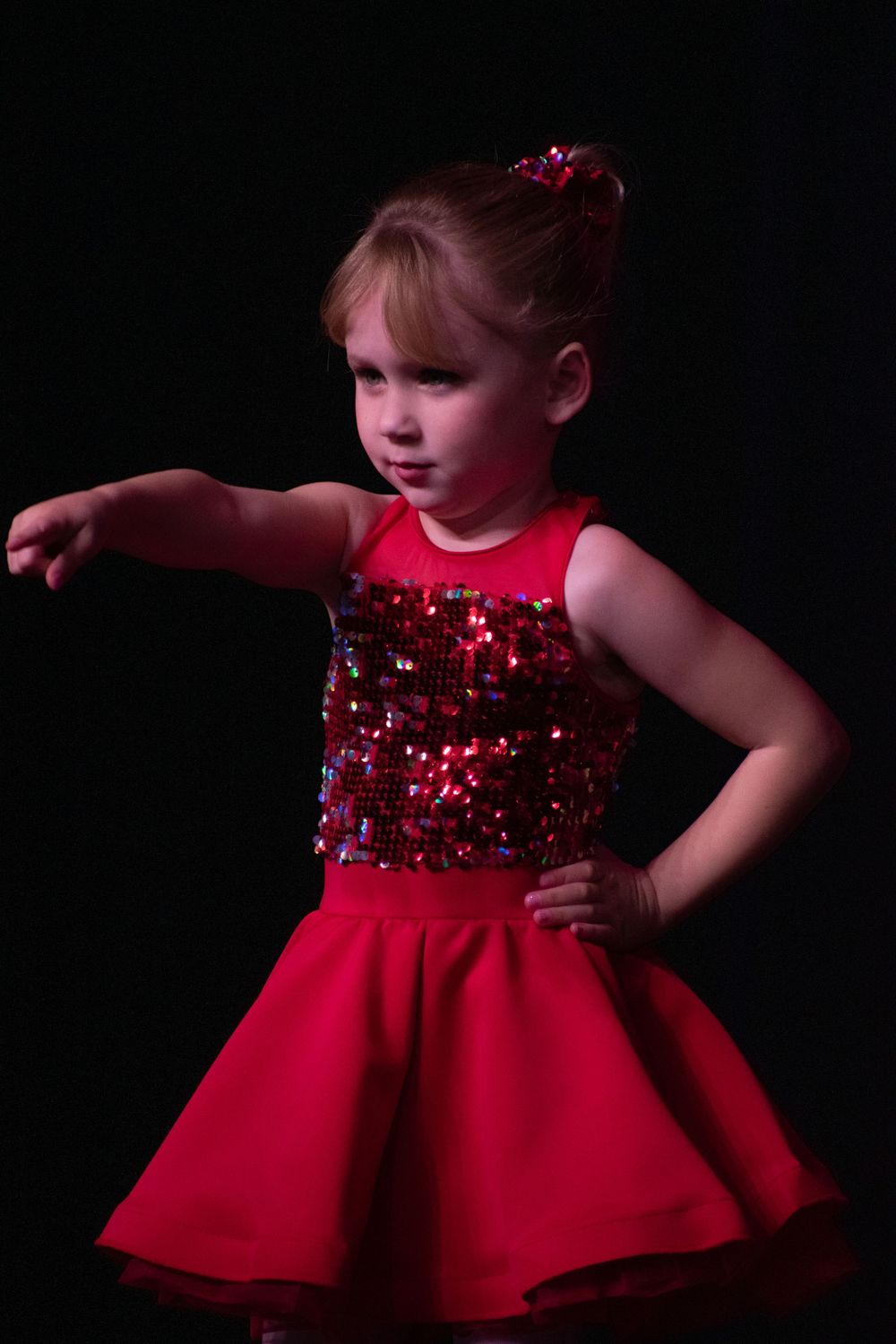 Dance performance featuring red dresses with sequined bodices on dark stage.