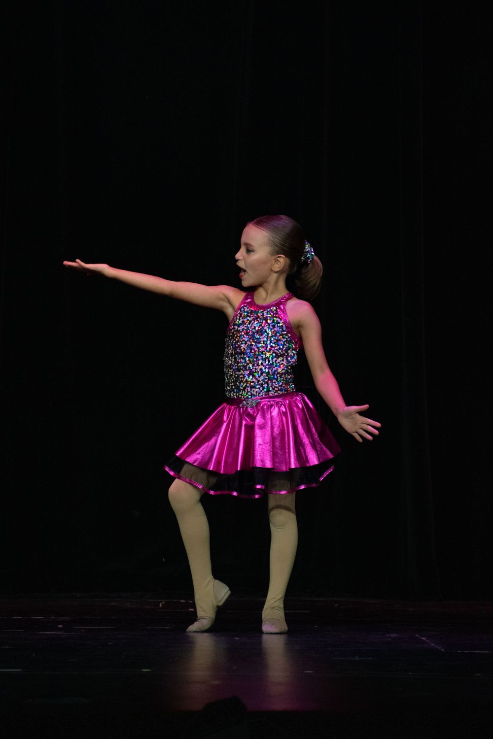 Dancers in bright pink dresses strike dramatic poses during stage performance.