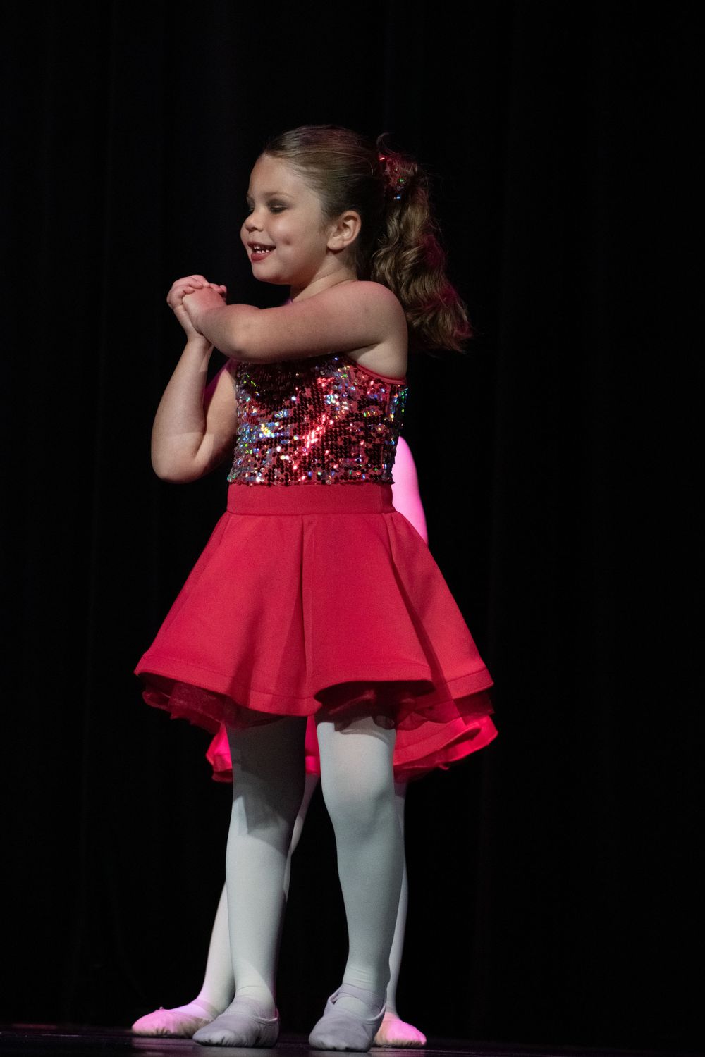 Dancers in red sparkly costumes and white tights perform on dark stage.