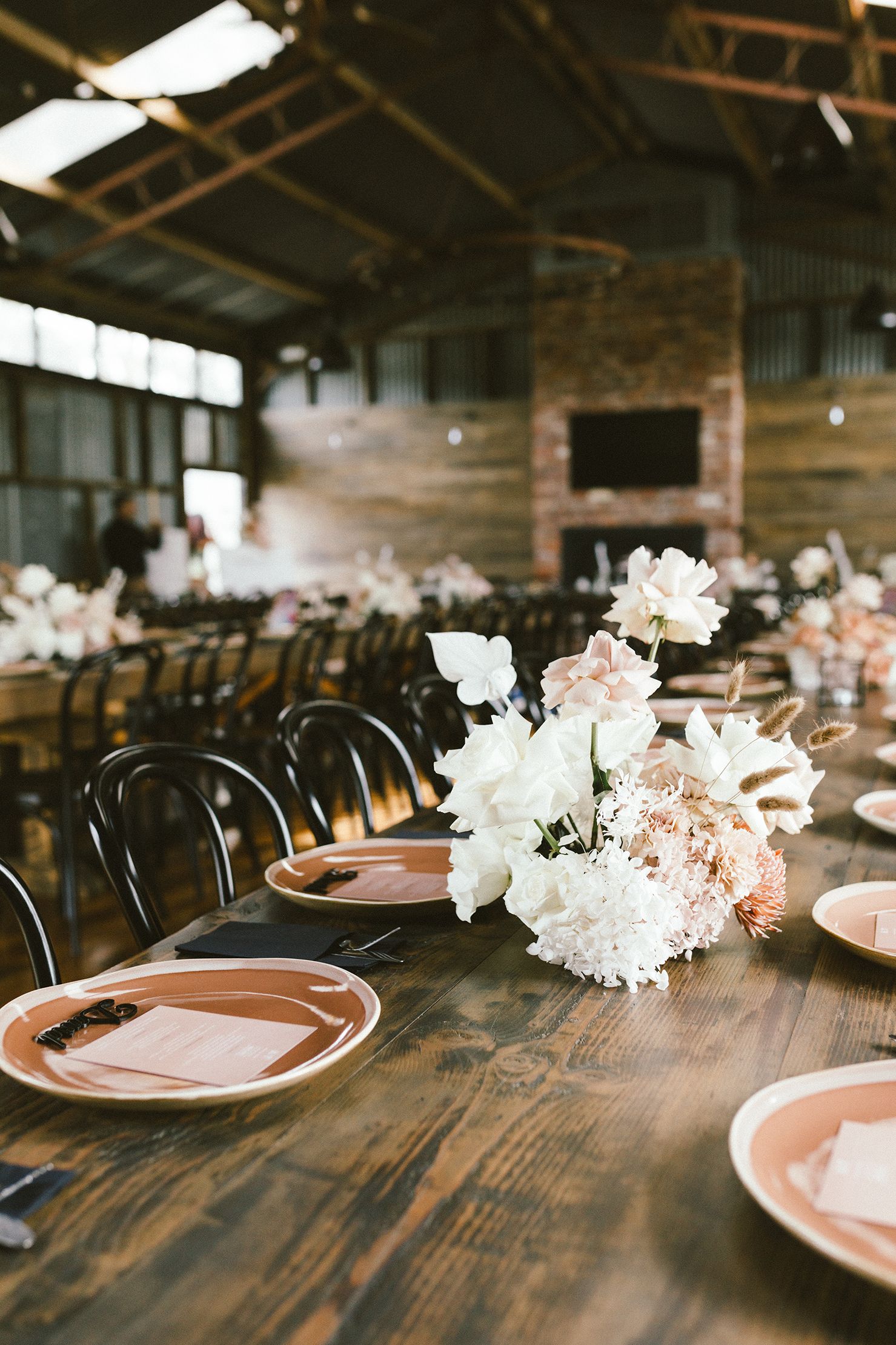 Elegant table setting with white floral centerpieces in a rustic reception venue.