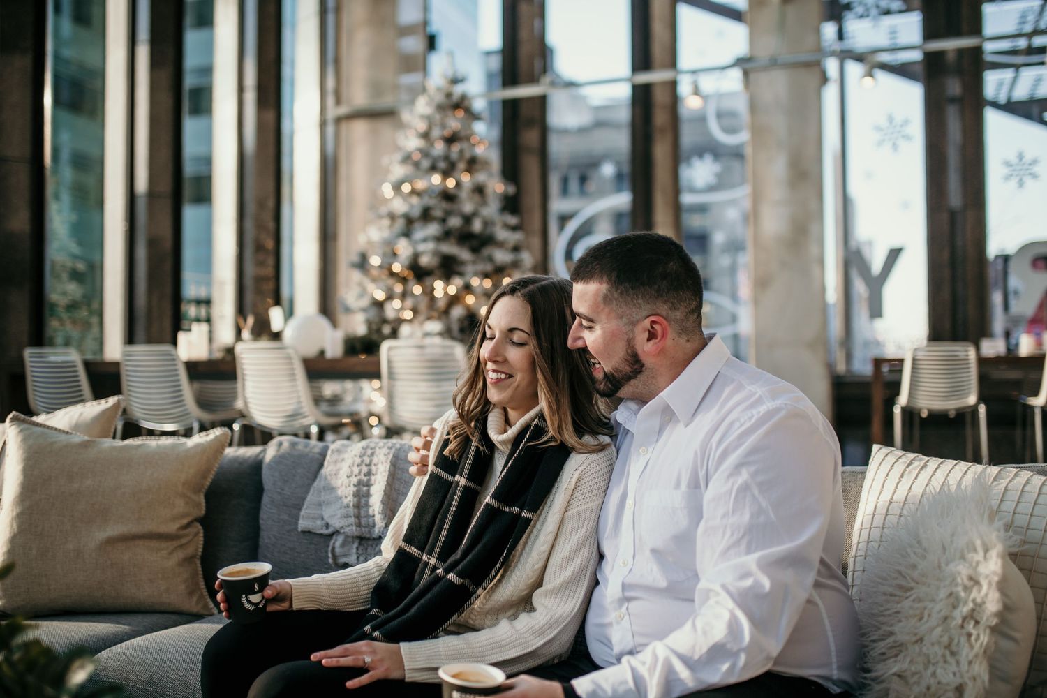 A couple relaxes on a couch in a modern lounge with a Christmas tree in the background.