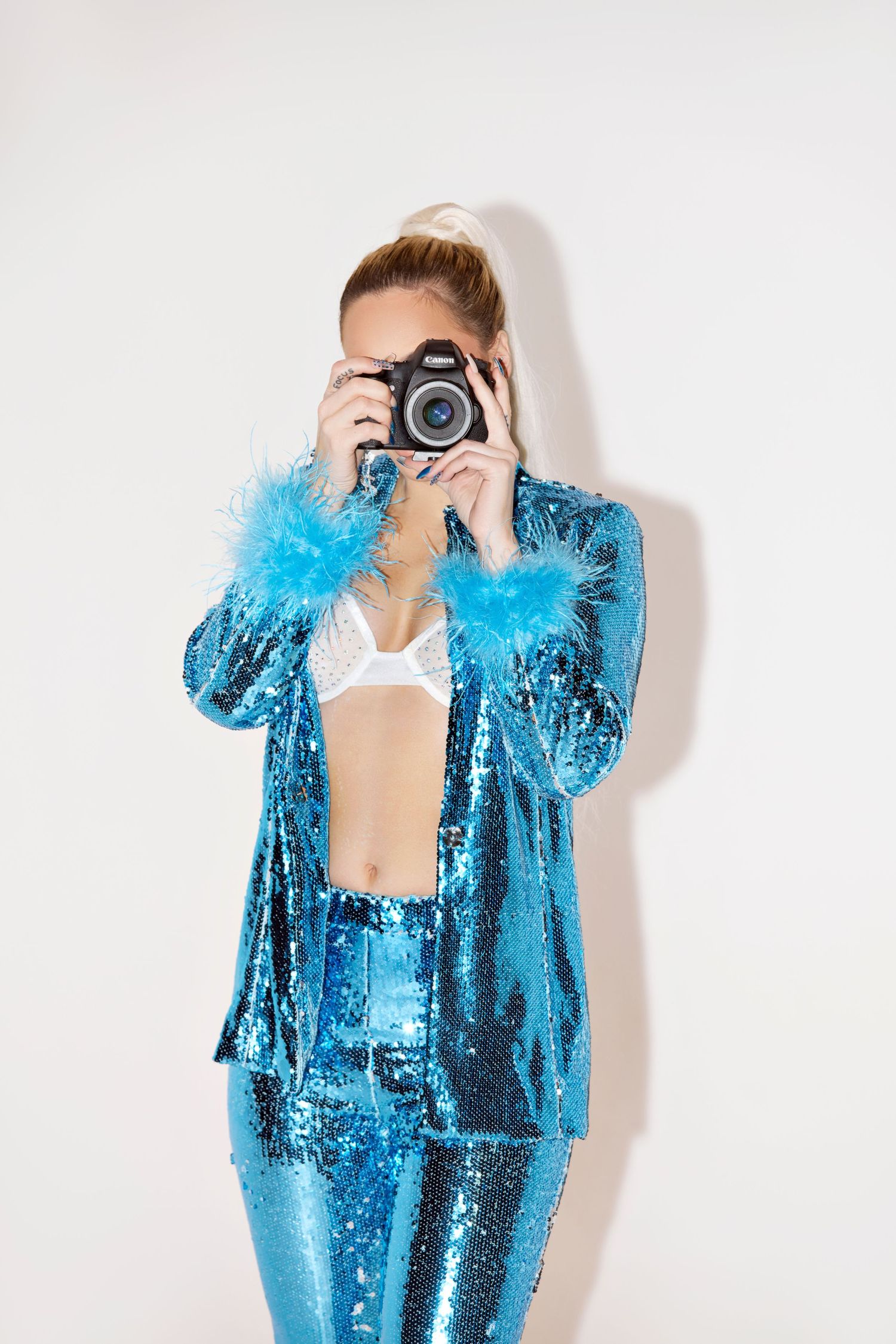Photographer in sparkling blue suit takes picture with professional camera against white wall.