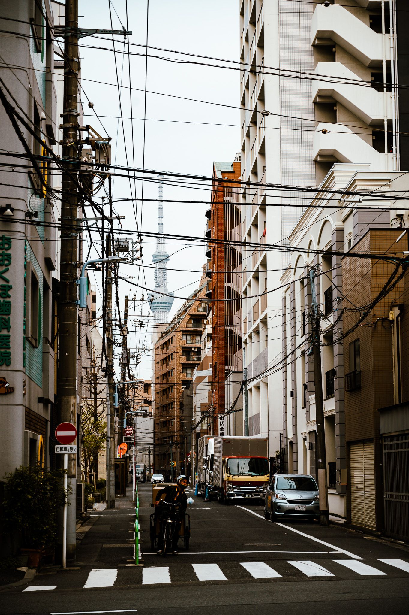 Urban street in Japan with dense power lines above and tall apartment buildings lining both sides.