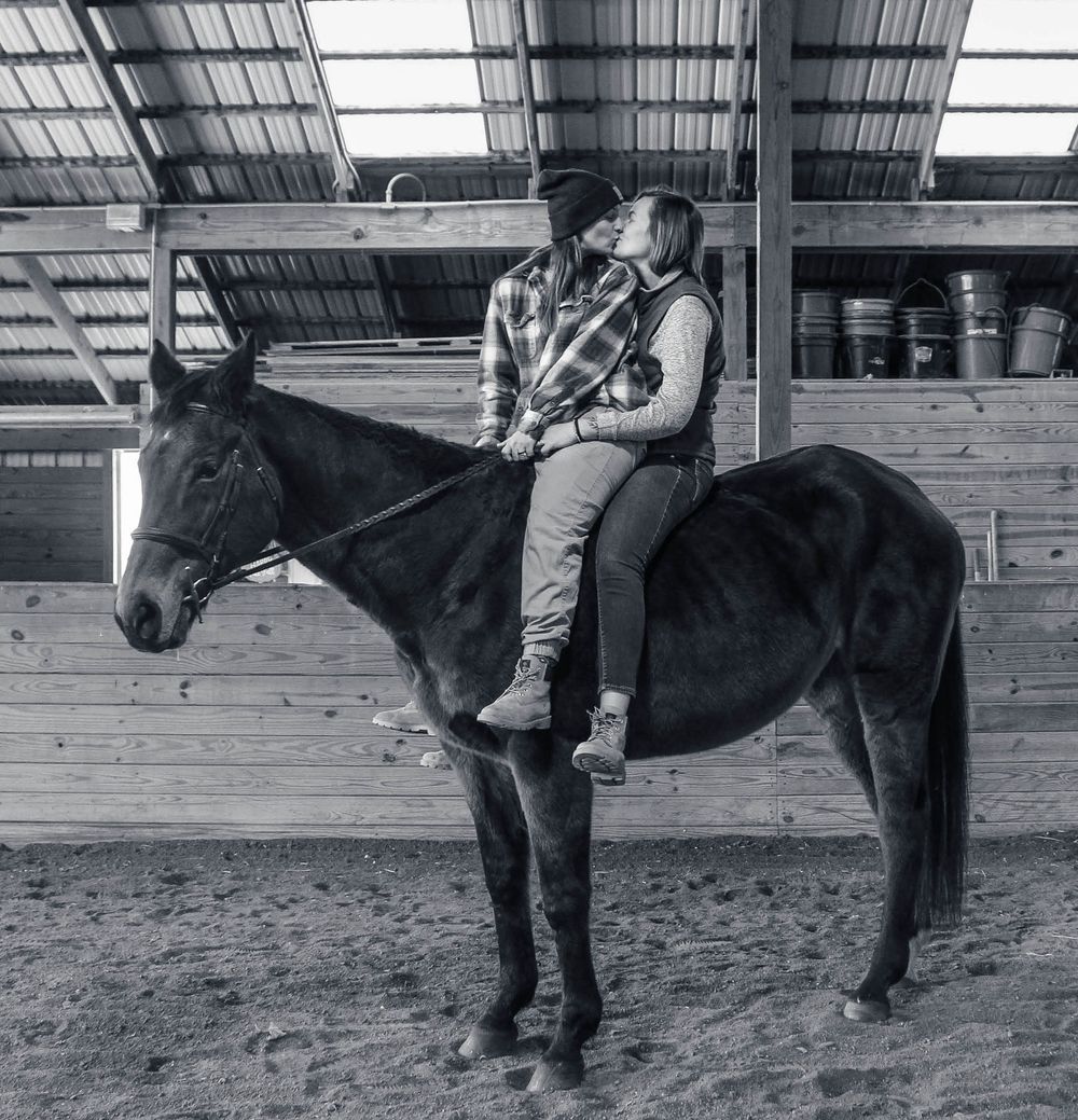 Black and white photo of a dark horse with rider in an indoor arena.