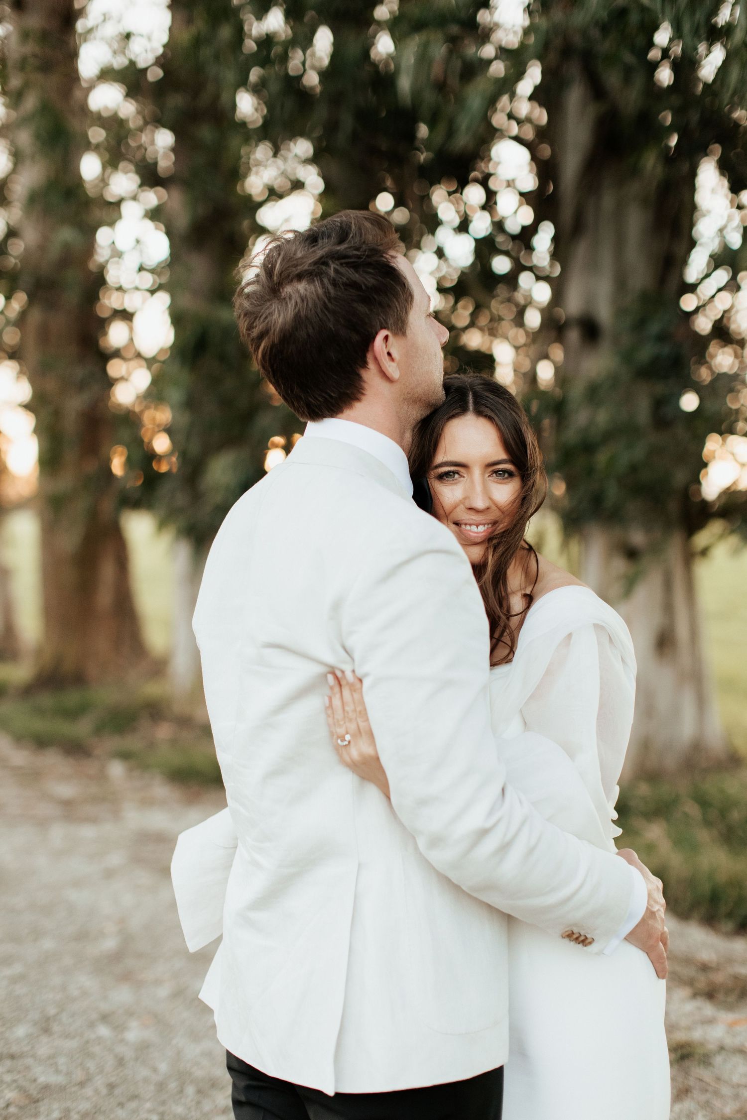 Romantic embrace between newlyweds under golden sunlight and trees.