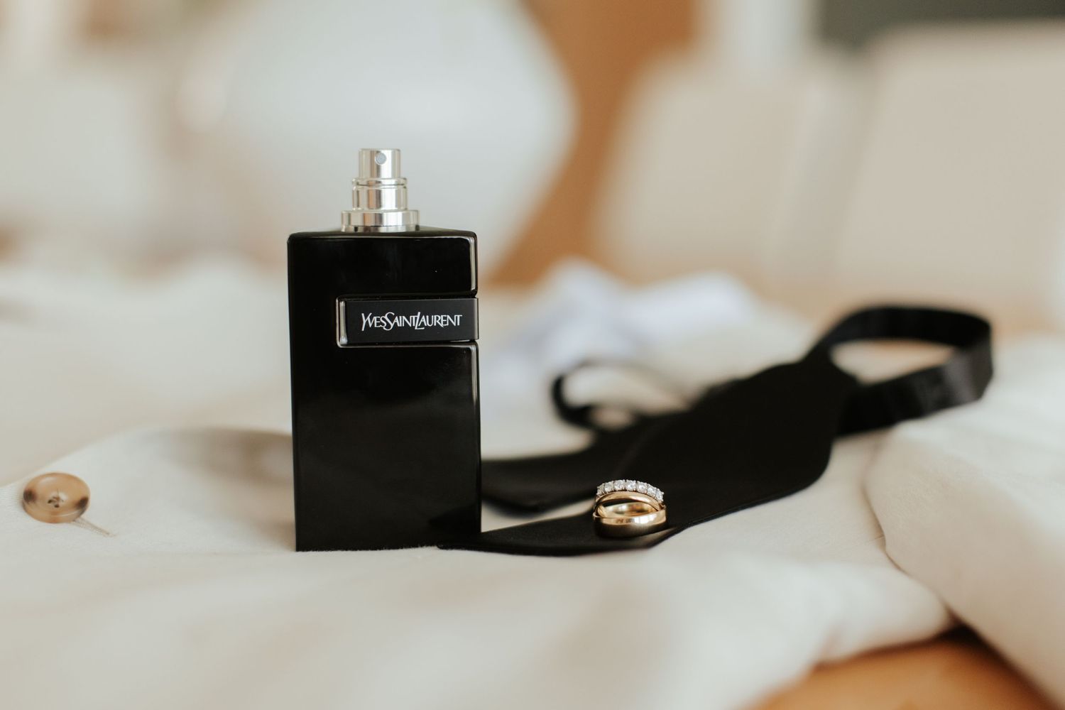 Black perfume bottle with strap on white fabric in soft focus.