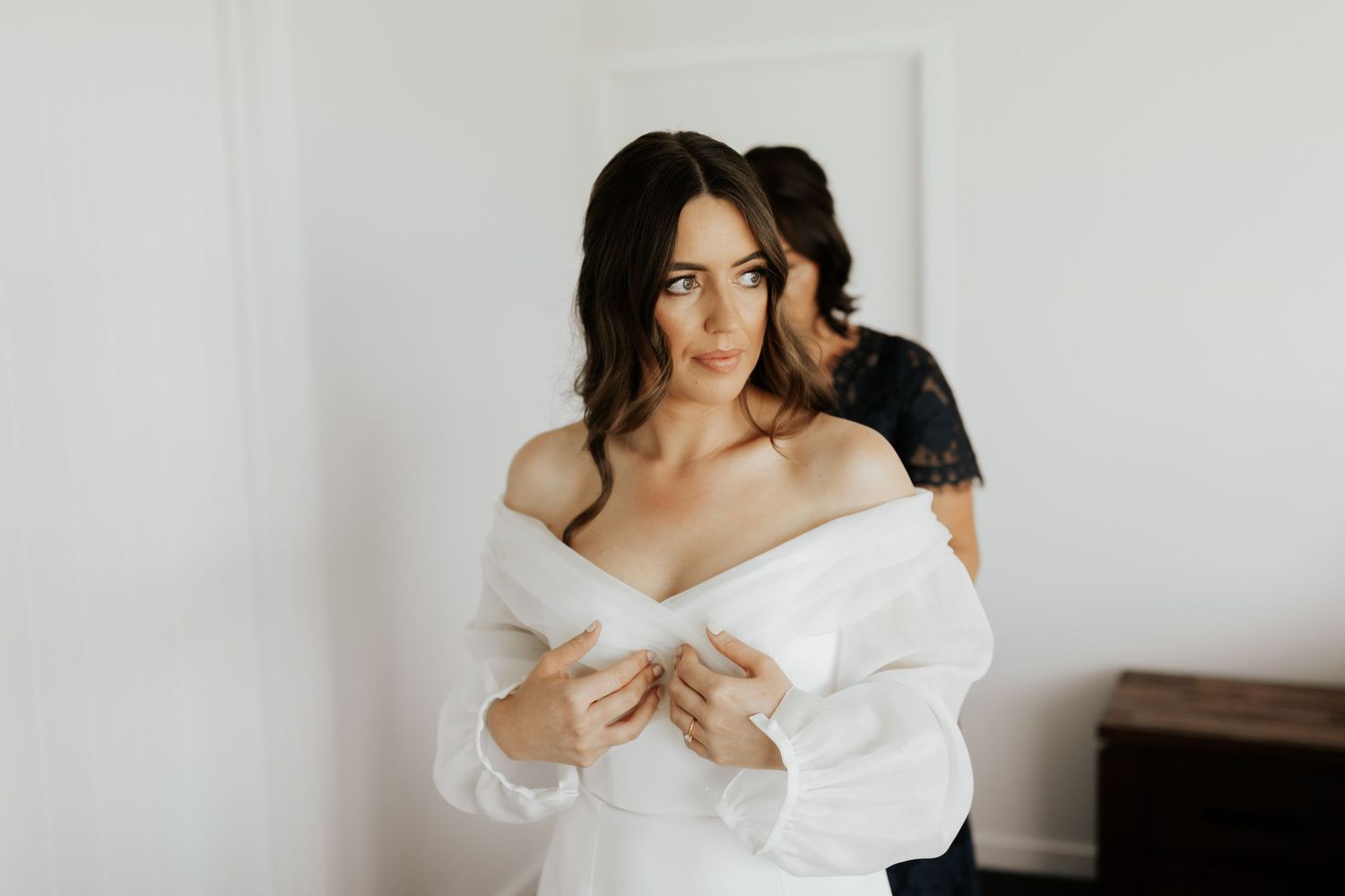 Elegant off-shoulder white dress being worn against minimal background.