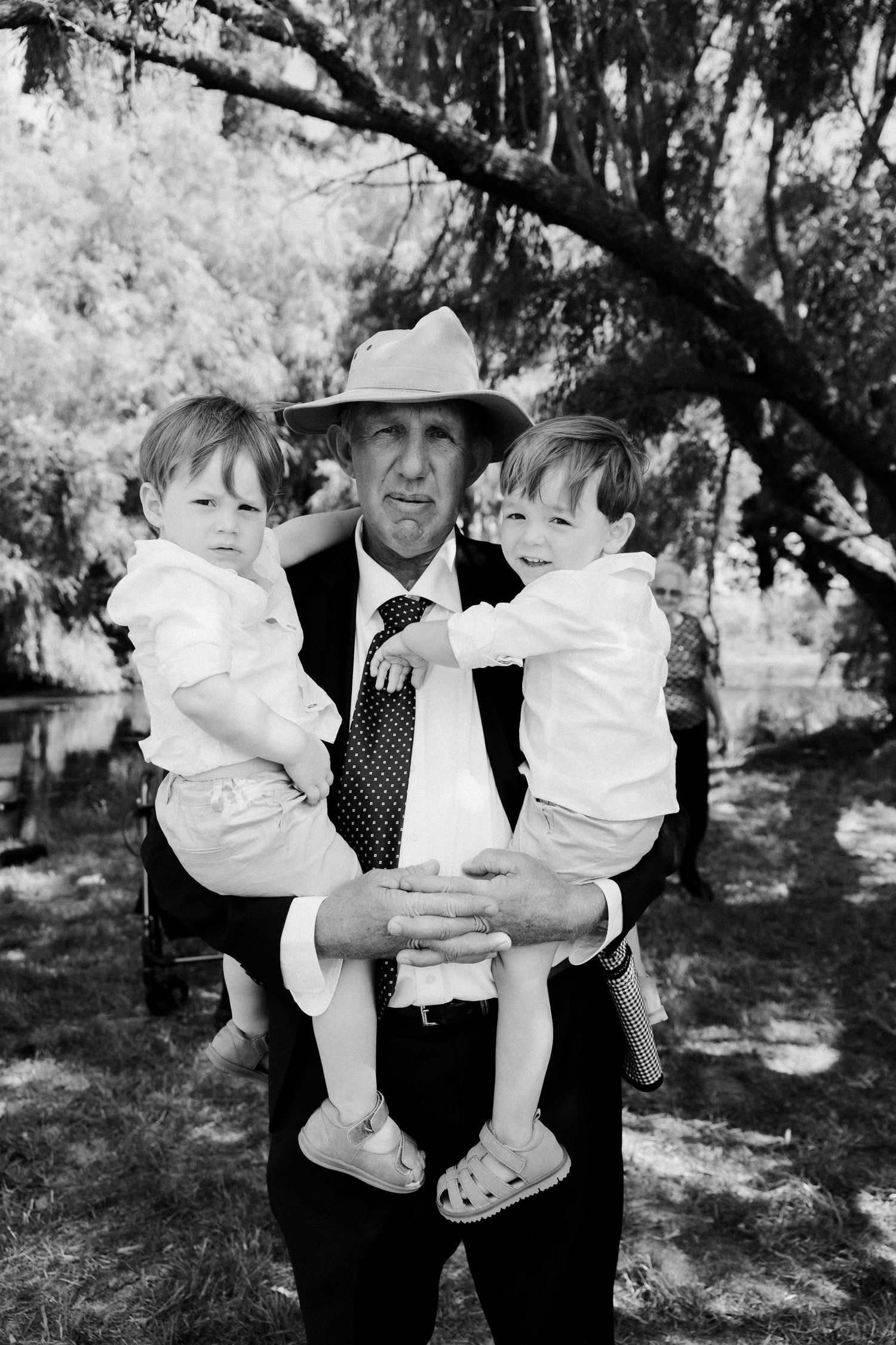 A black and white portrait of an older gentleman in a hat holding two young children outdoors.