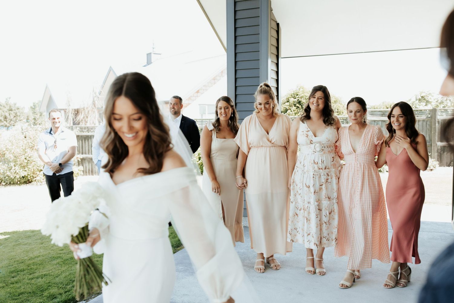 Bridal party in assorted light colored dresses walking outdoors.