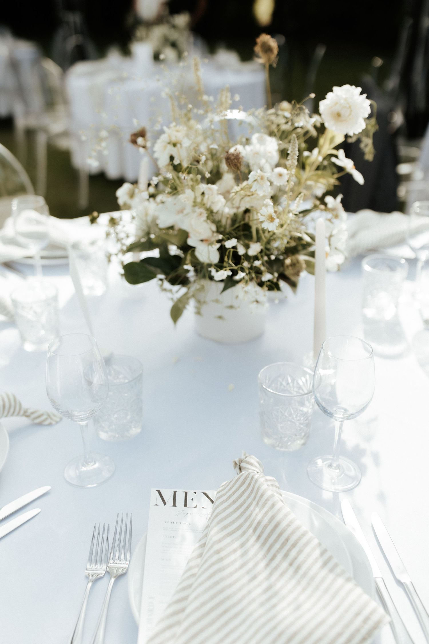 Elegant white floral centerpiece on reception table with striped napkin and crystal glassware.