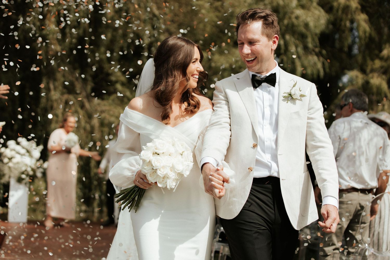 Newlyweds walking through confetti shower during outdoor wedding celebration.