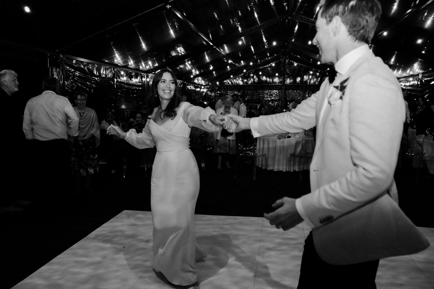 Wedding couple dancing on a white dance floor under twinkling lights in black and white.