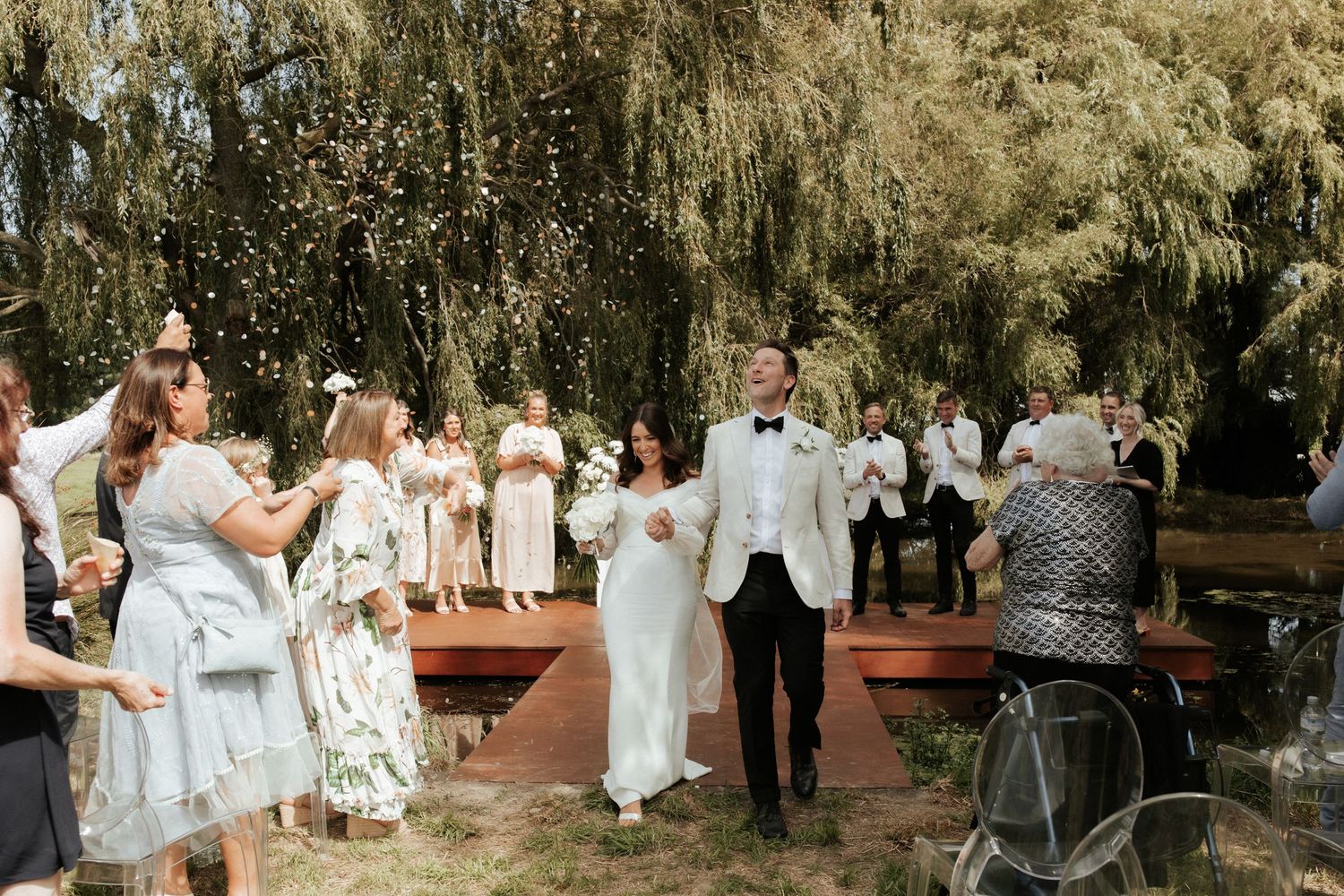Wedding guests celebrating and throwing confetti during outdoor ceremony.