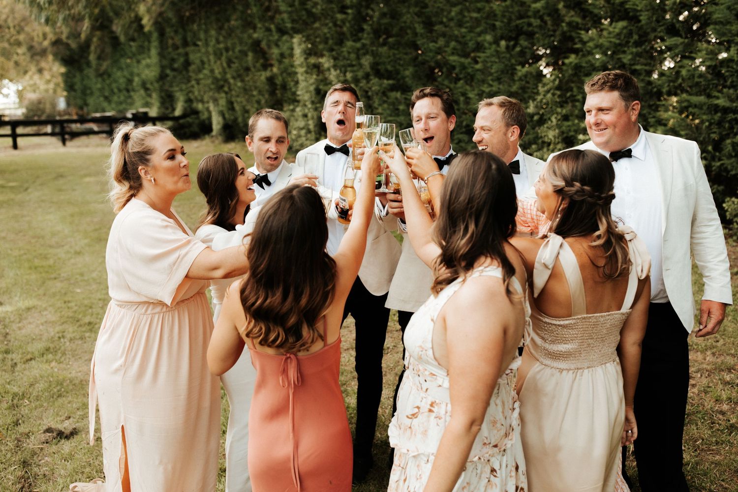 Wedding party celebrates with champagne toasts outdoors during a sunny celebration.