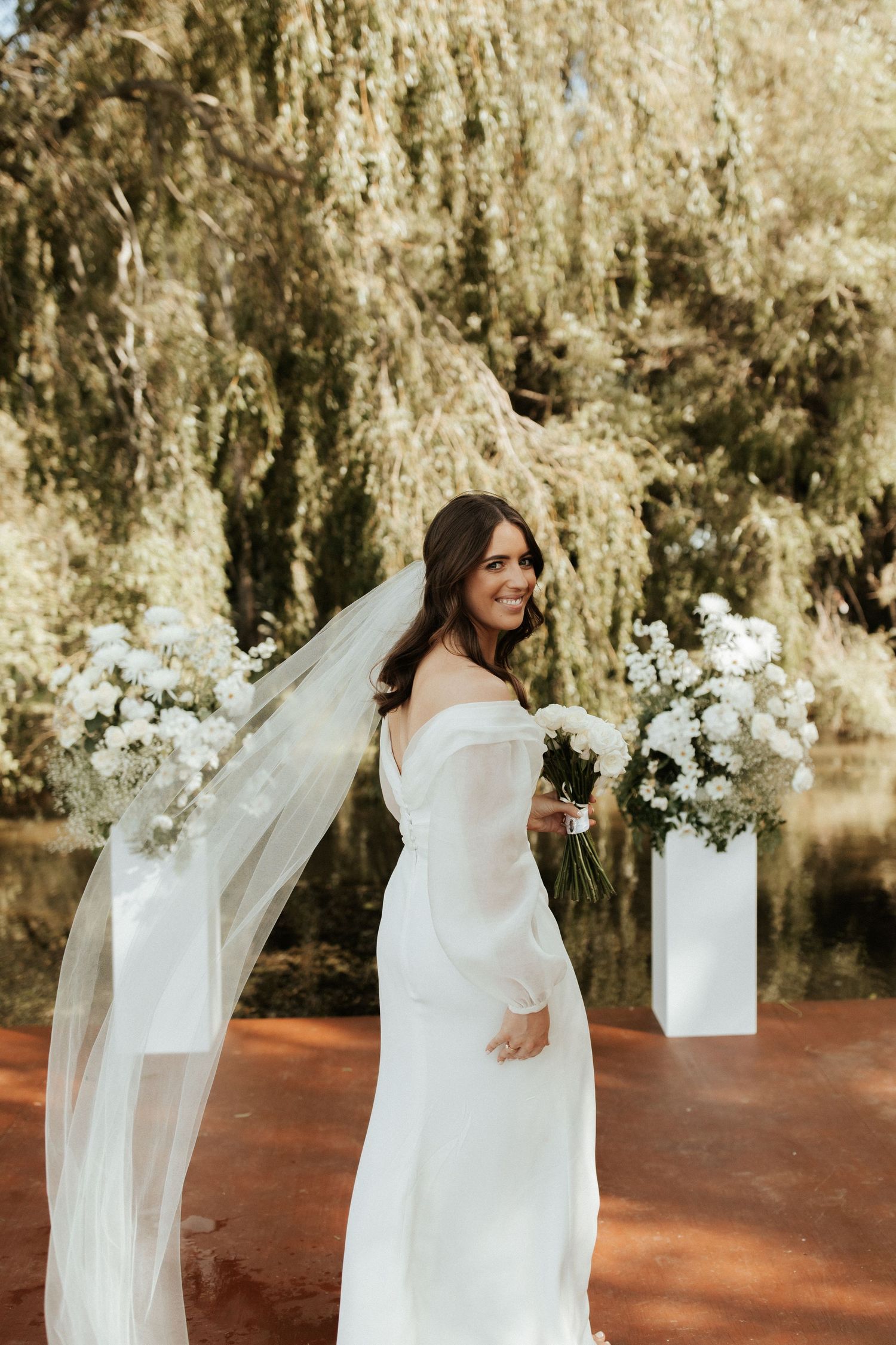 A bride in a flowing white gown poses elegantly with her veil and bouquet.