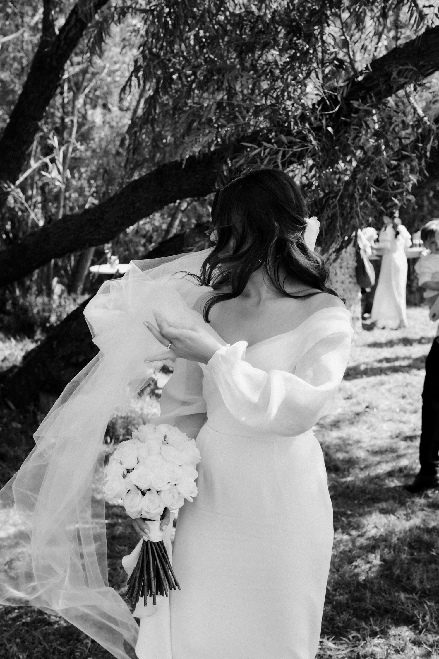 Black and white portrait of bride holding white bouquet under willow tree.