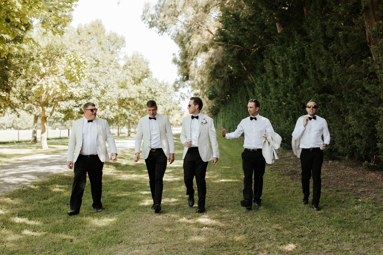 Group of groomsmen walking together in white jackets and black pants.