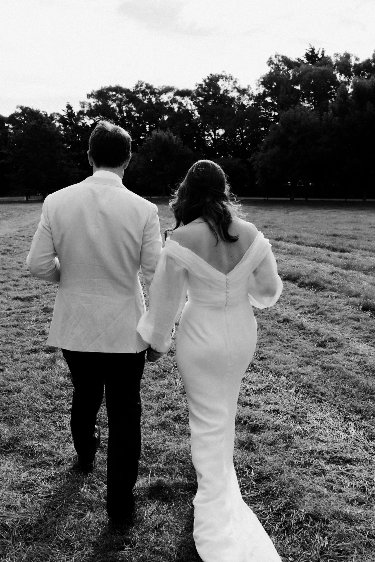 Black and white photo of couple walking together in formal attire across an open field.
