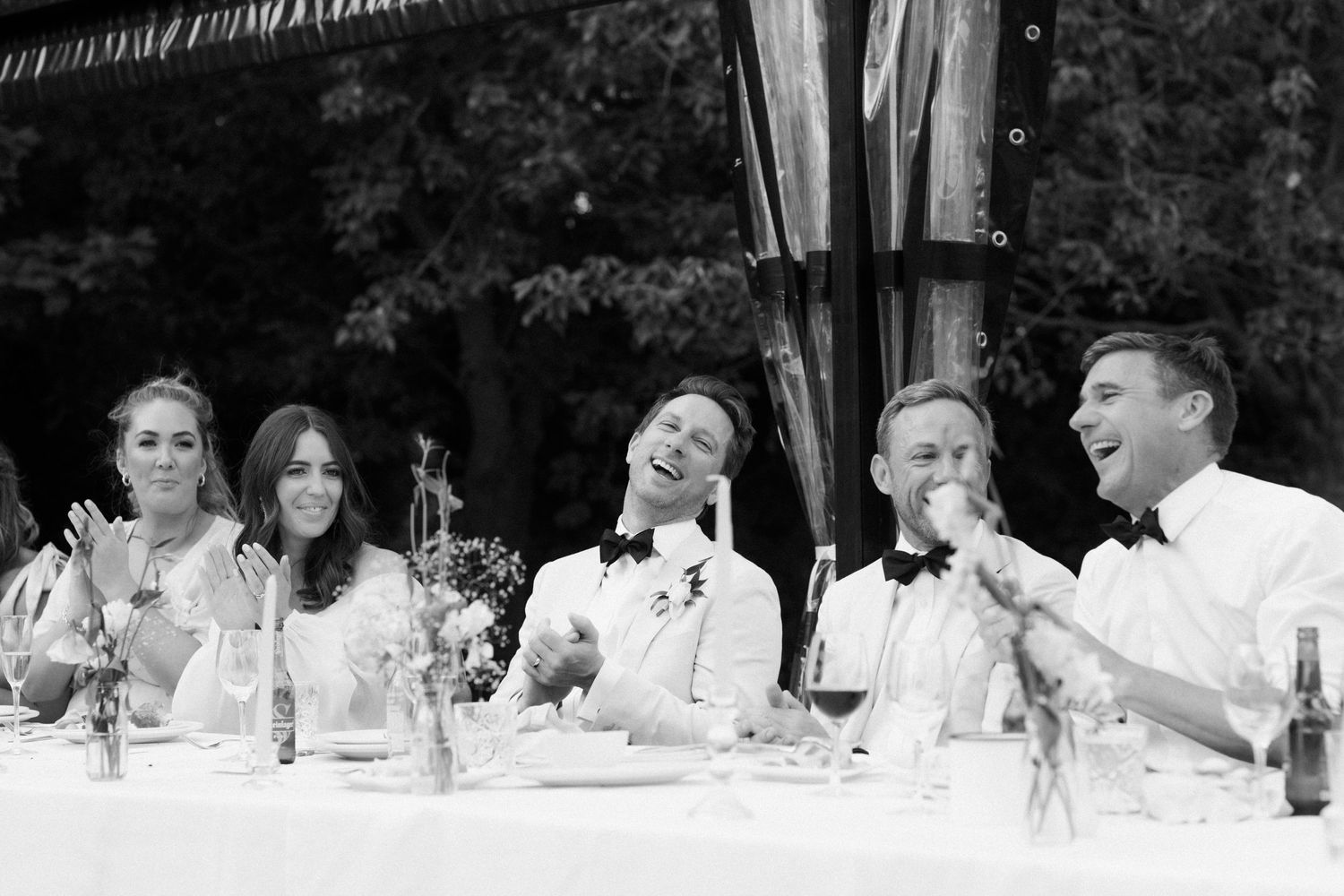 Wedding guests laughing joyfully at an outdoor reception dinner table.
