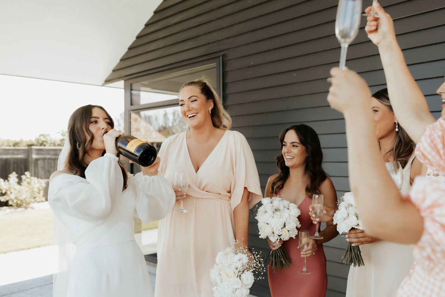 Wedding party celebrates with champagne on a porch in front of a dark gray house.